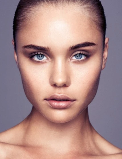 Close-up studio portrait of a young adult female with fair skin, light blue eyes, and light brown hair against a soft grey backdrop.