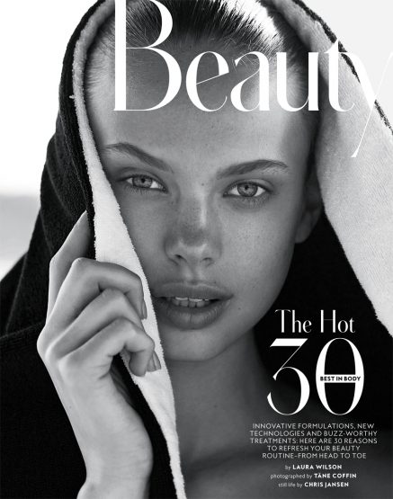 Black and white beauty shot of a young woman wearing a black hooded towel and looking directly at the camera in a close-up shot.