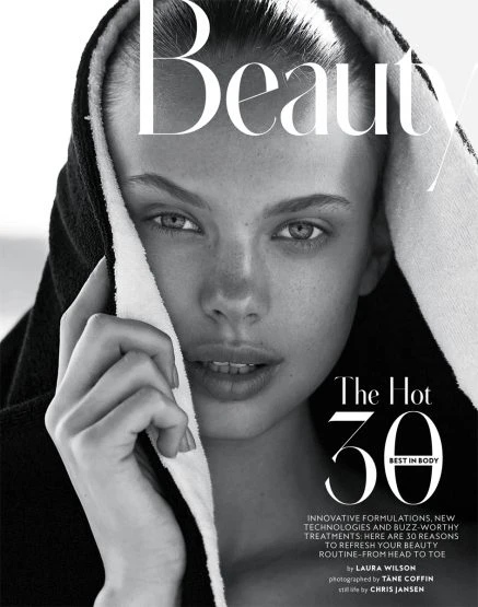 Black and white beauty shot of a young woman wearing a black hooded towel and looking directly at the camera in a close-up shot.
