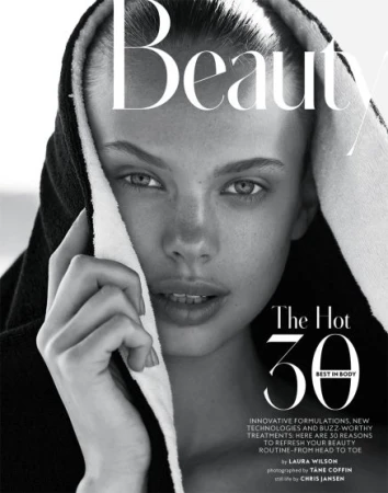 Black and white beauty shot of a young woman wearing a black hooded towel and looking directly at the camera in a close-up shot.