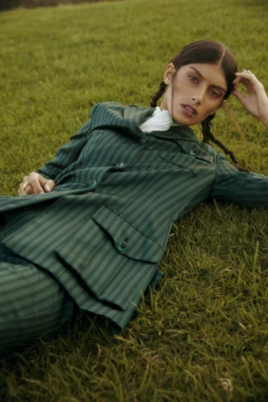 Model lying on grass wearing a green patterned jacket with braided hair and natural makeup by Joel Phillips