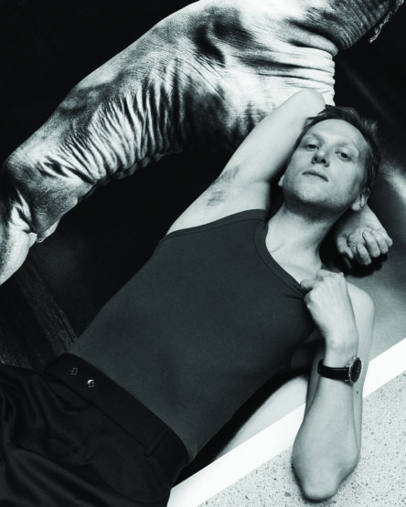 Monochrome portrait of a man in a dark tank top lying down with an arm raised near a patterned surface in Sydney.