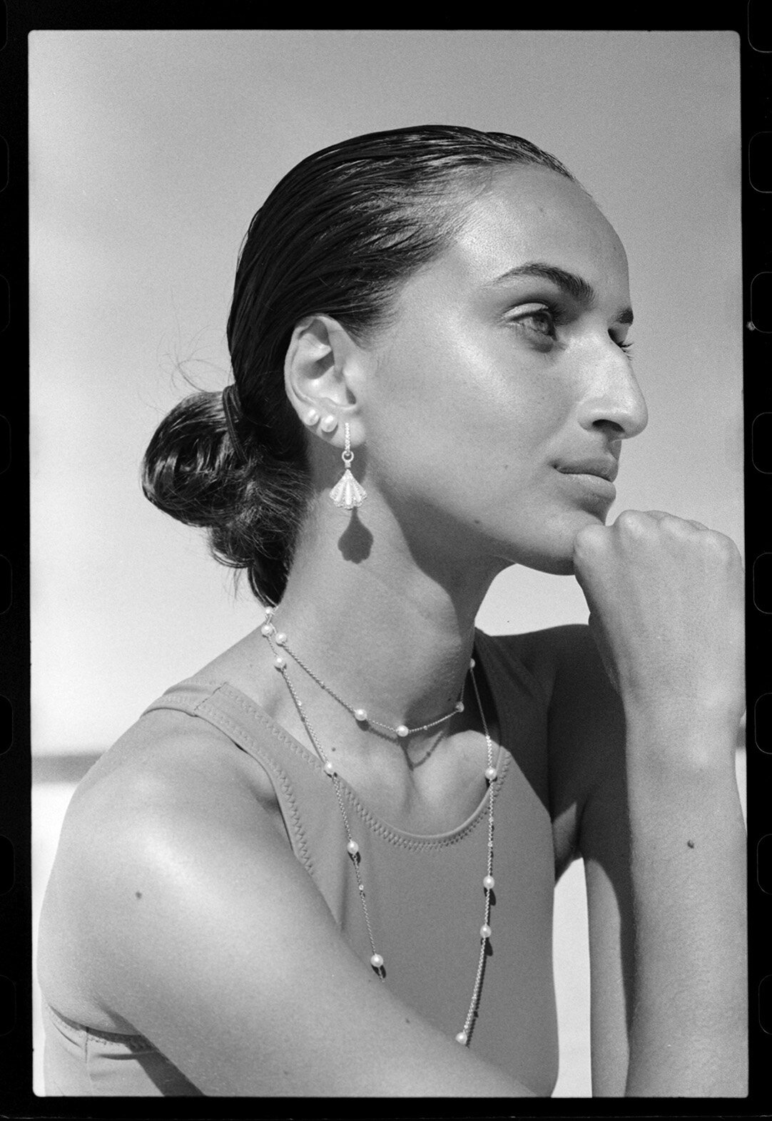Black and white portrait of a woman in profile wearing layered pearl necklaces and shell drop earrings by photographer Max Doyle.