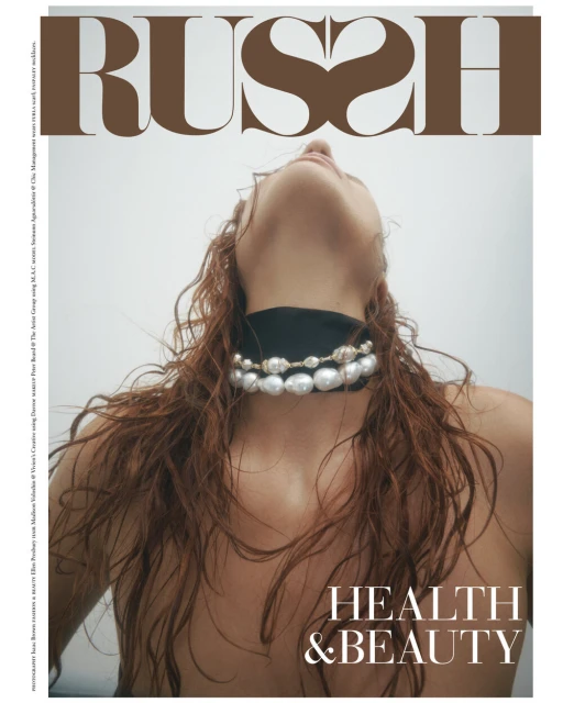 Magazine cover shot at a low angle featuring a red-haired woman wearing pearl choker against a light background. The magazine title 'RUSH' is displayed.