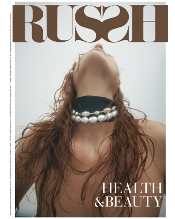 Magazine cover shot at a low angle featuring a red-haired woman wearing pearl choker against a light background. The magazine title 'RUSH' is displayed.