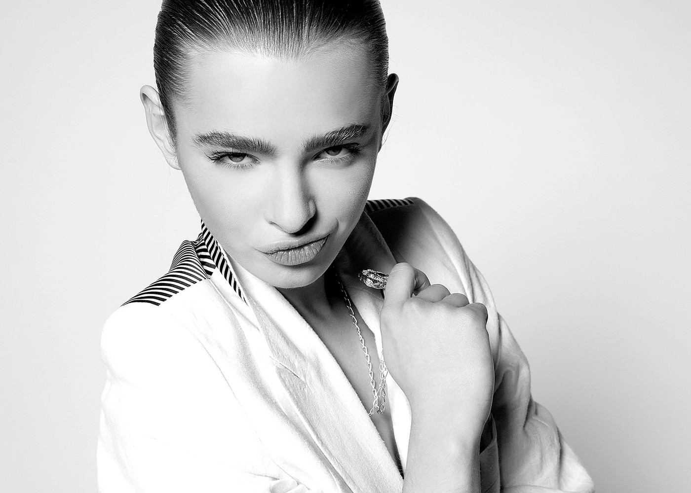 Black and white portrait of an adult female wearing a white blazer with a striped collar and necklace, posing in a photo studio.