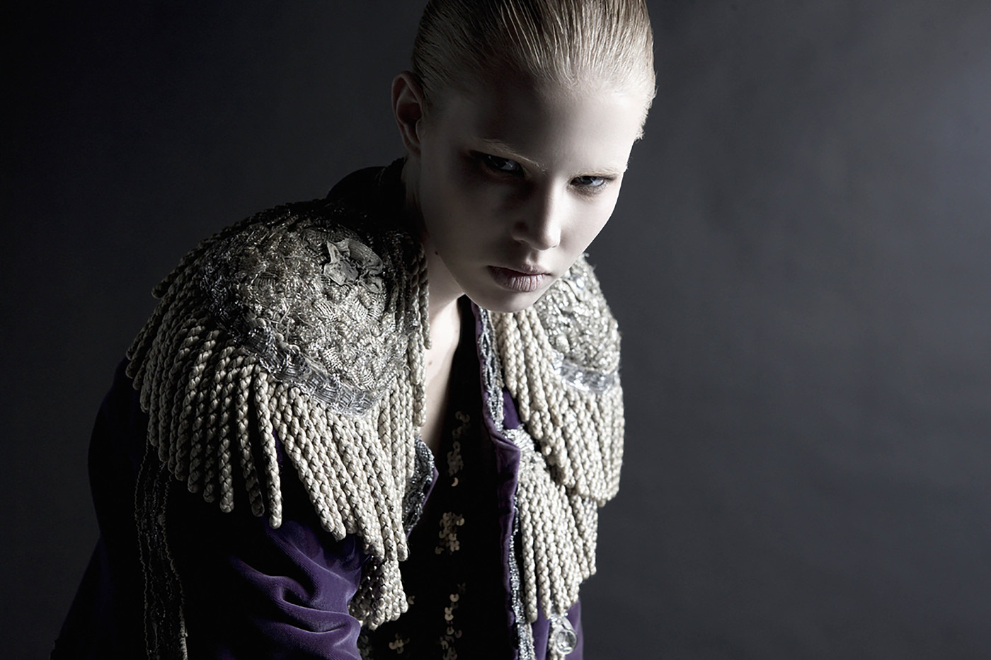 Portrait of a fair-skinned woman in a dark photo studio, wearing a purple velvet jacket with ornate silver shoulder embellishments.