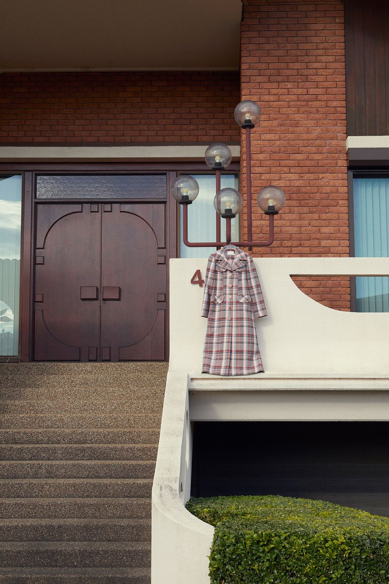 Eye-level shot of a plaid coat hanging outside on a lamp post next to a brick building with concrete stairs in daylight.