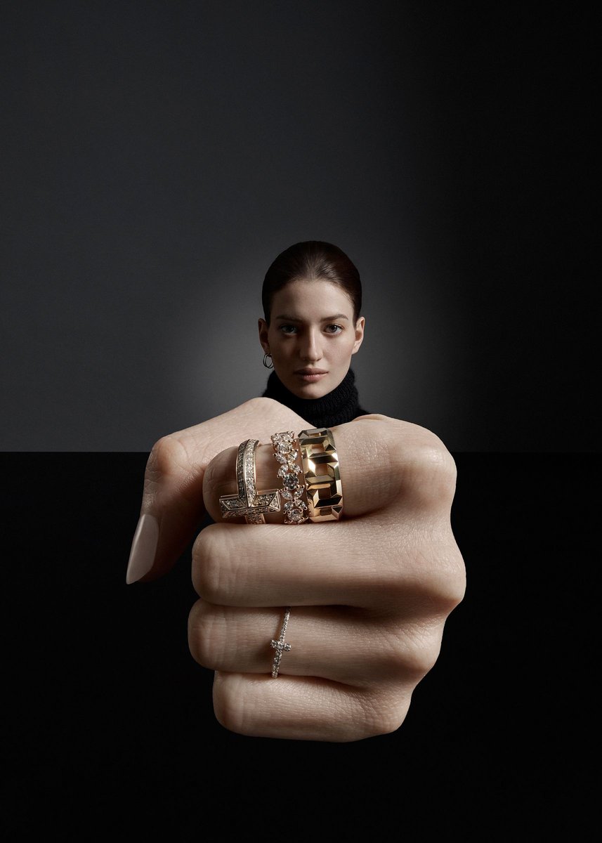 Close-up studio shot of a woman with various gold and diamond rings on her fingers against a dark gray and black background.