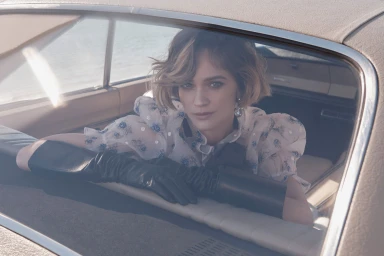 Woman wearing sheer floral blouse and long black leather gloves looking through car rear window by photographer Juli Balla