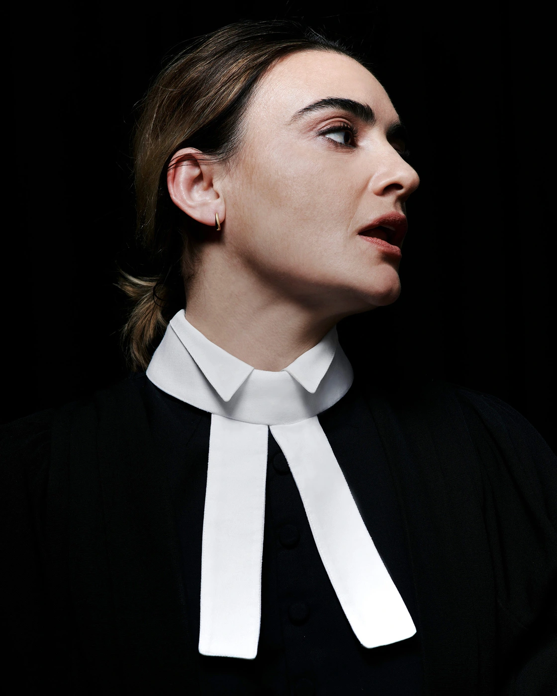 Portrait of a woman wearing a black garment with a white clerical collar against a dark background