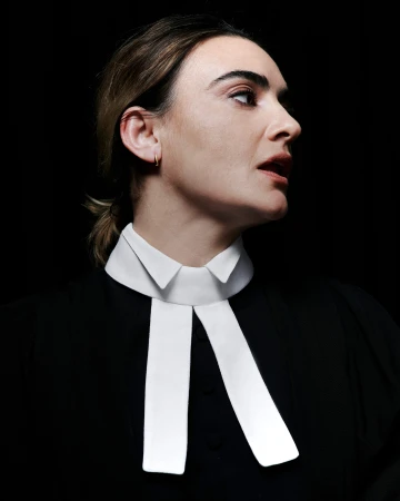 Portrait of a woman wearing a black garment with a white clerical collar against a dark background