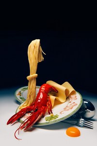 Lobster and spaghetti on a decorative plate, studio shot with creative lighting and a black backdrop, showcasing food photography.