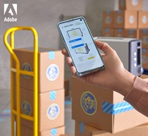 Close-up shot of a person holding a smartphone displaying a graphic, next to stacked cardboard boxes with circles in a storage room.