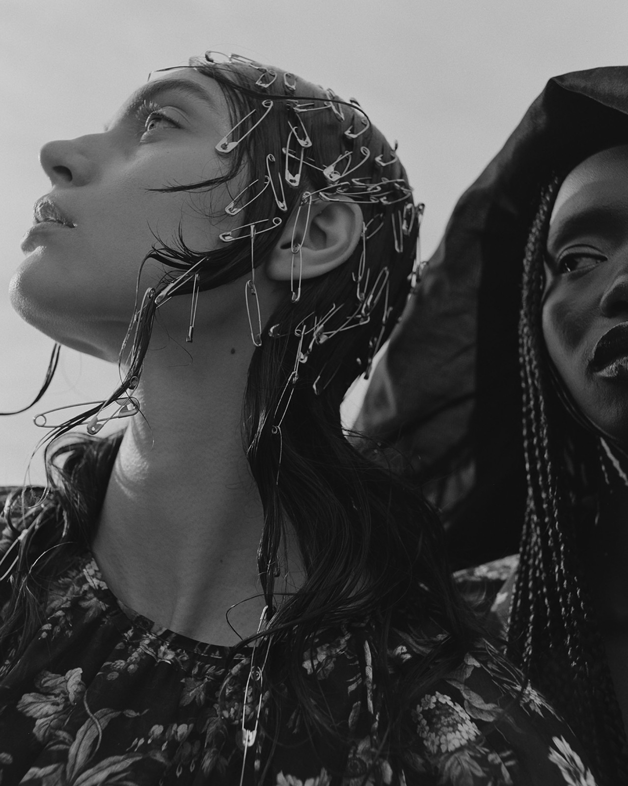 Monochrome portrait of two women, one with safety pins in her hair, against a bright sky. Fashion and beauty concept.