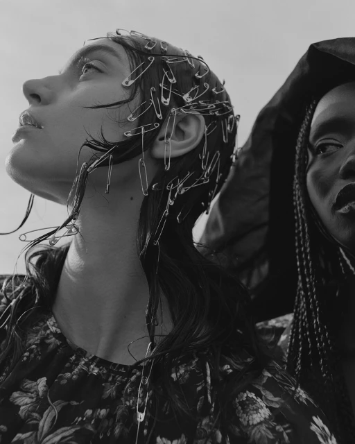 Monochrome portrait of two women, one with safety pins in her hair, against a bright sky. Fashion and beauty concept.
