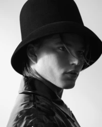 Close-up portrait of a man wearing a dark felt hat and black jacket against a bright seamless background by Jake Terrey