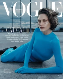 Model Catherine McNeil wearing a bright blue catsuit posing on a concrete rooftop under an overcast sky.