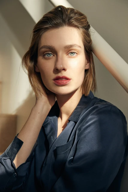Close-up studio shot of an adult female with blue eyes and short brown hair wearing a collared blue-gray shirt. Neutral studio background.