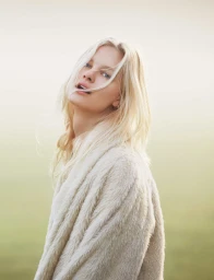 Portrait of a blonde woman wearing a textured cream cardigan against an out of focus outdoor background