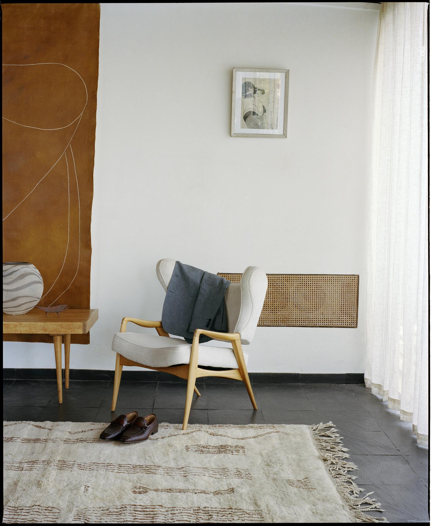 Interior design featuring a wingback chair, a side table with ceramic vase, a woven rug, and a modern artwork on a white wall.