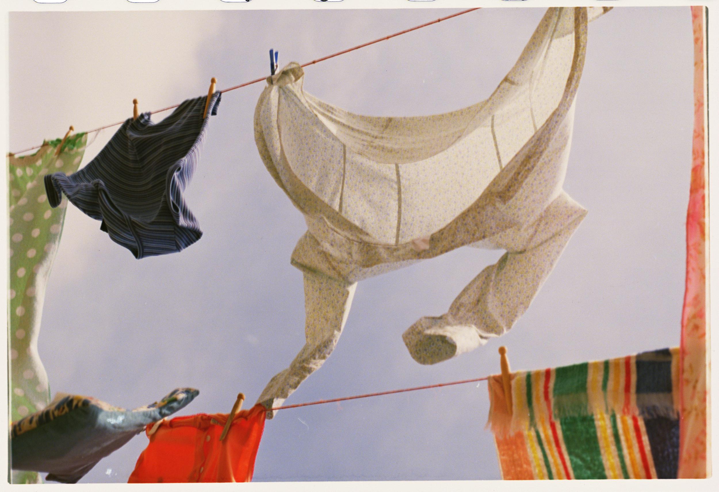 Clothes hanging on a line, suspended against a bright sky with visible clothespins, creating a domestic, breezy, and colorful scene.