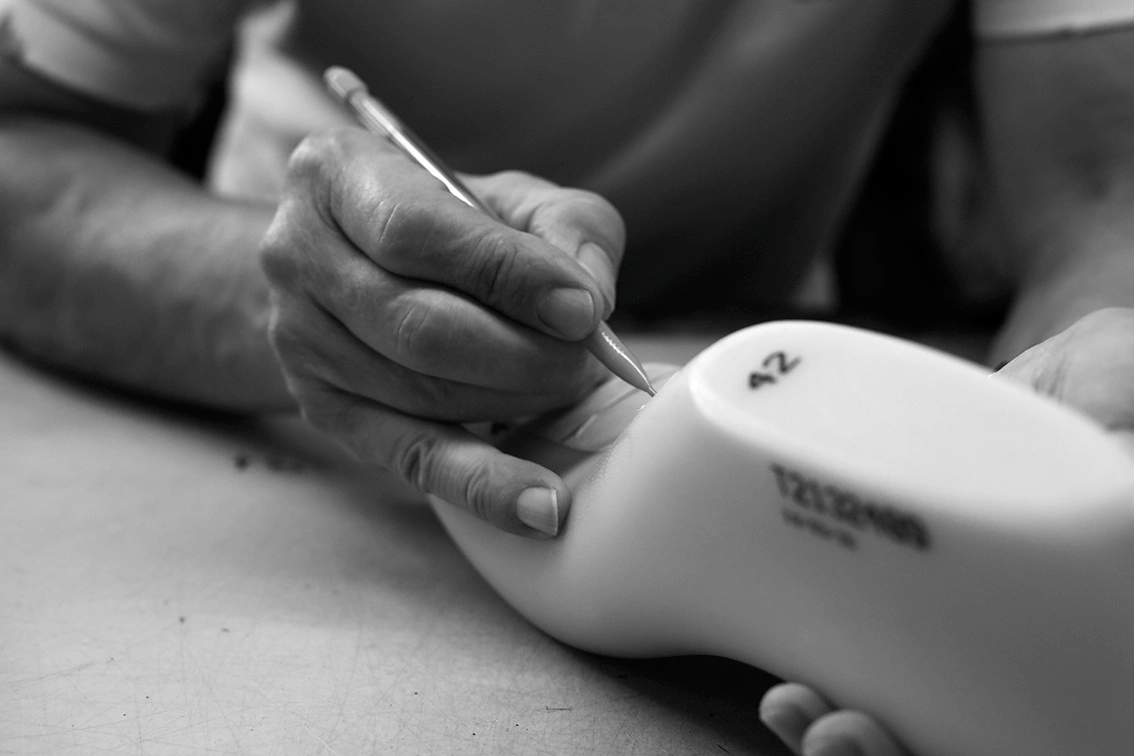Close-up of hands writing on a shoe last with a pencil in a workshop setting