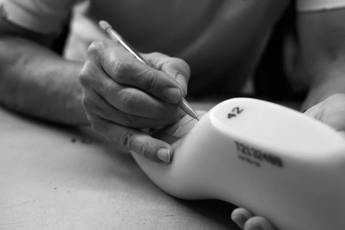 Close-up of hands writing on a shoe last with a pencil in a workshop setting