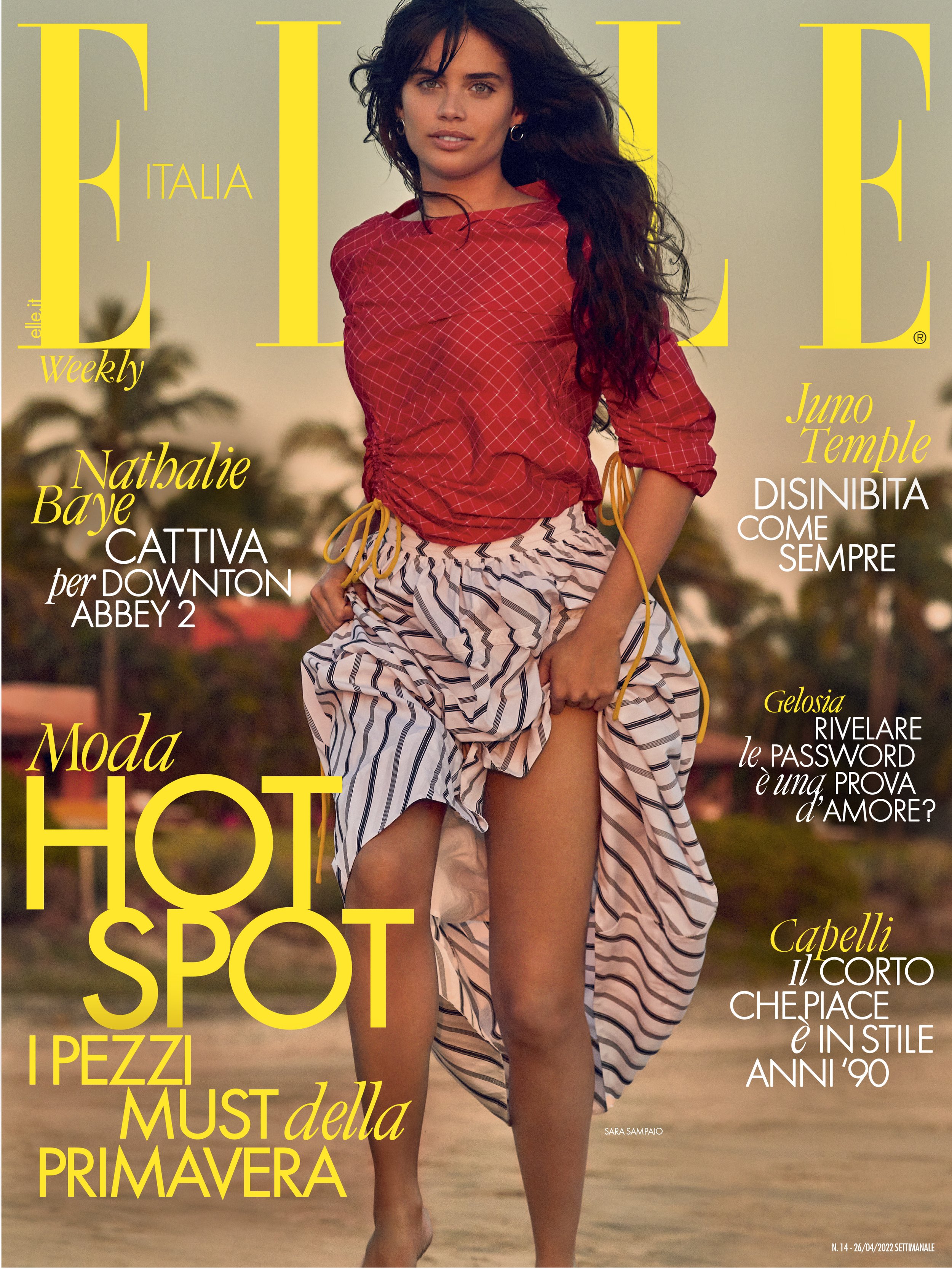 Elle Italia magazine cover featuring a woman in a red top and striped skirt, posing on a beach with text overlays and brand logo.