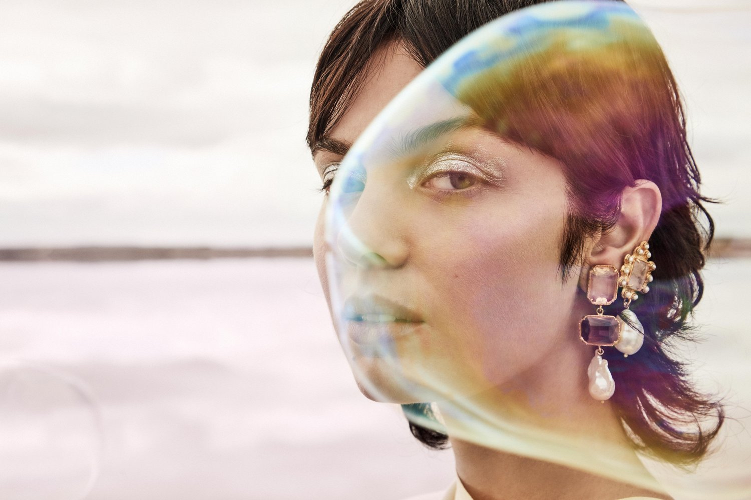 Close-up portrait of a stylish adult woman with an earring, artistic color shift, and soft focus, against a blurred outdoor background.