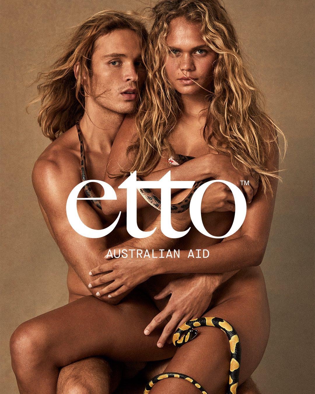 Nude couple embraces; a brown snake is coiled around their legs. The “etto” brand name is large in front of the tan background.