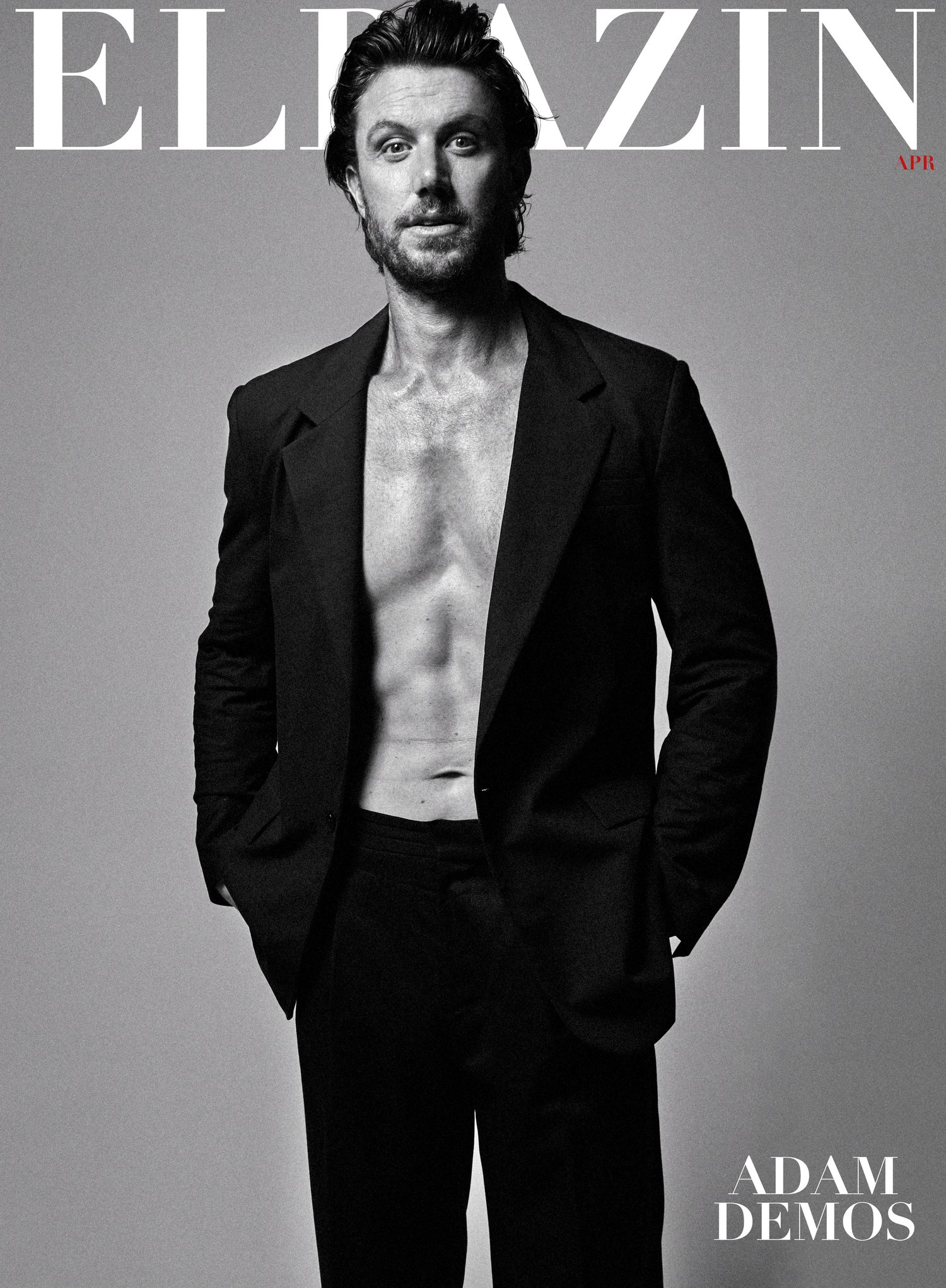 Portrait of a shirtless man in a black blazer against a neutral background, with a magazine masthead visible at the top.