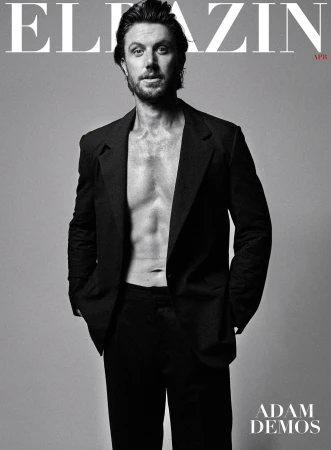Portrait of actor Adam Demos wearing an open dark suit jacket against a grey background photographed by Simon Upton