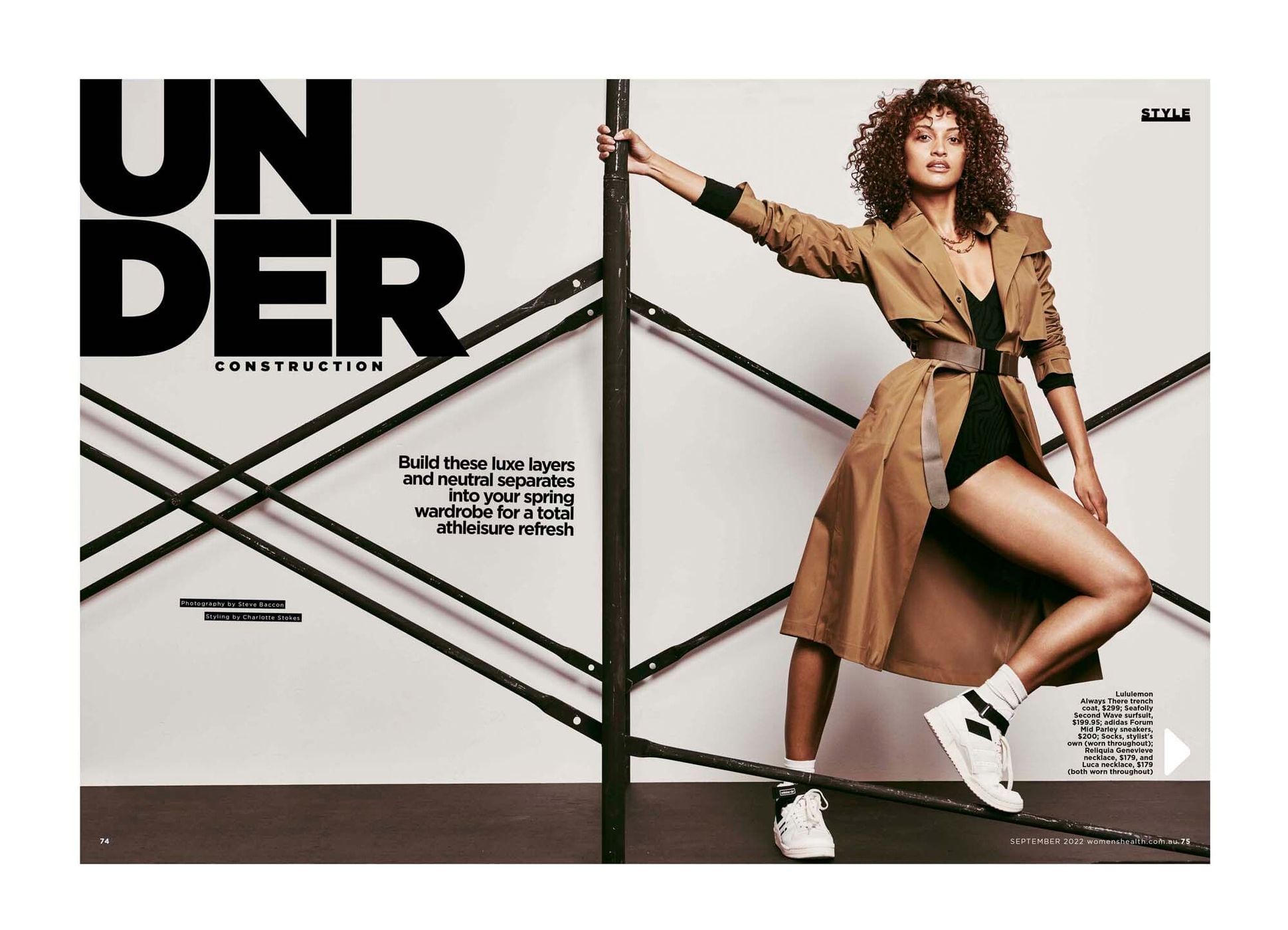 Fashion editorial shot of an adult woman with curly hair wearing a trench coat with a black bodysuit, white socks, and sneakers.
