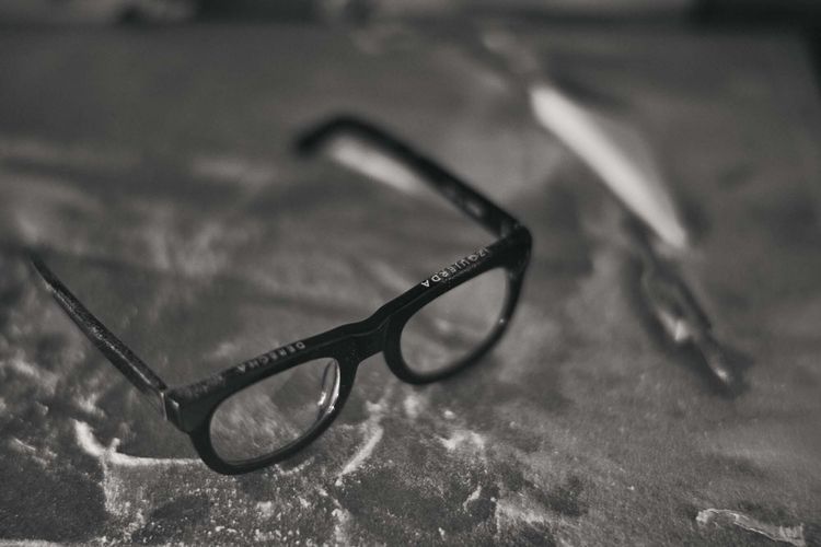 Black eyeglasses with arms resting on a textured surface, close-up shot in black and white with shallow depth of field.