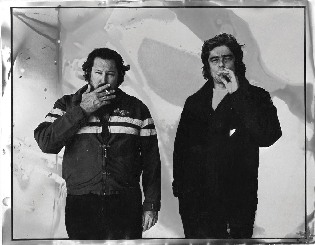 Black and white portrait of two men smoking cigarettes against a textured abstract backdrop by Ben Watts