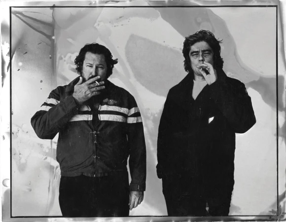 Black and white portrait of two men smoking cigarettes against a textured abstract backdrop by Ben Watts