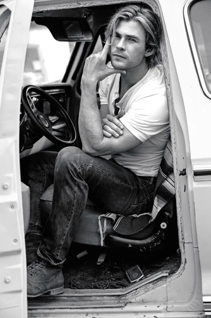 Black and white portrait of a light-skinned adult male sitting in the driver's seat of an old truck, leaning his arm on the door.