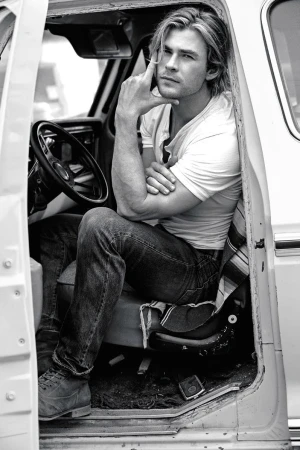 Black and white portrait of a light-skinned adult male sitting in the driver's seat of an old truck, leaning his arm on the door.