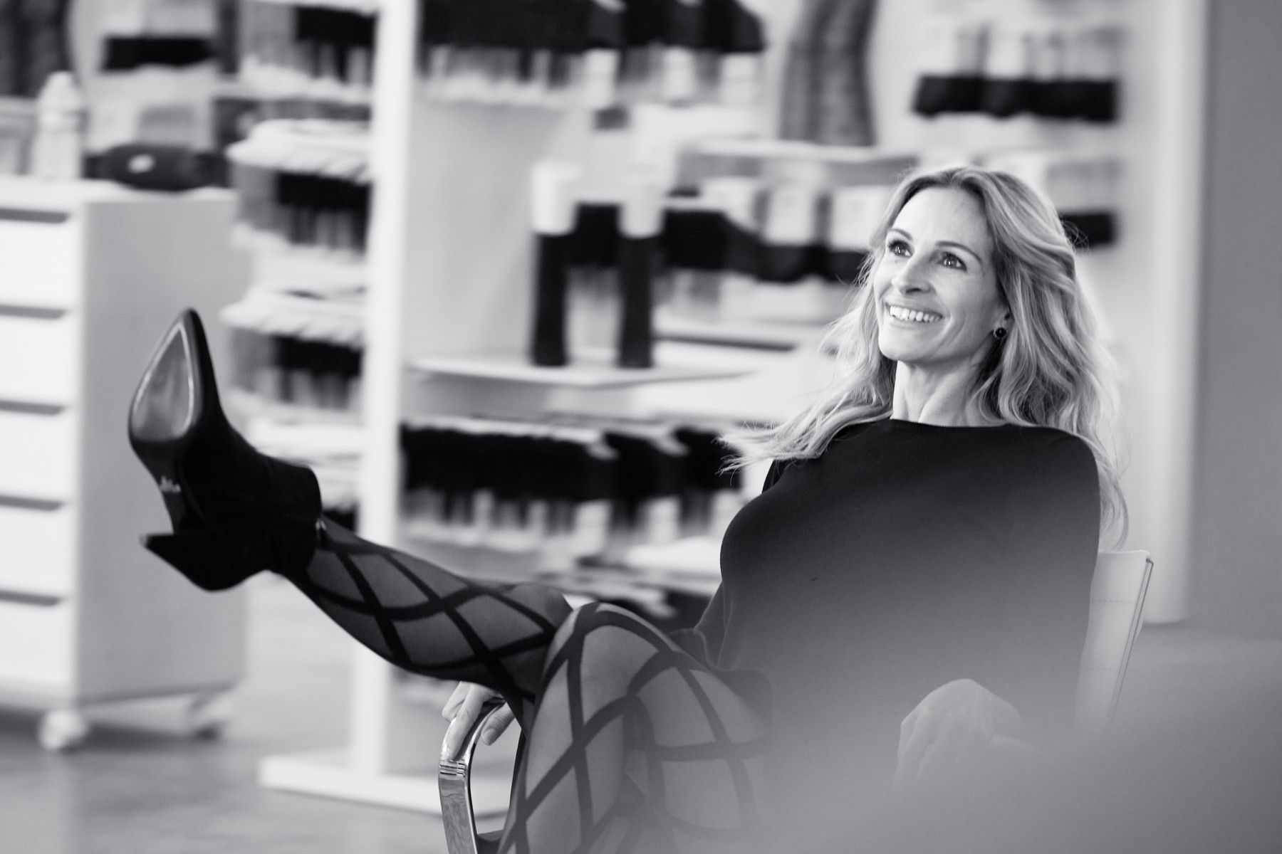 Julia Roberts seated with legs kicked up wearing patterned tights and high heels in a black and white photograph