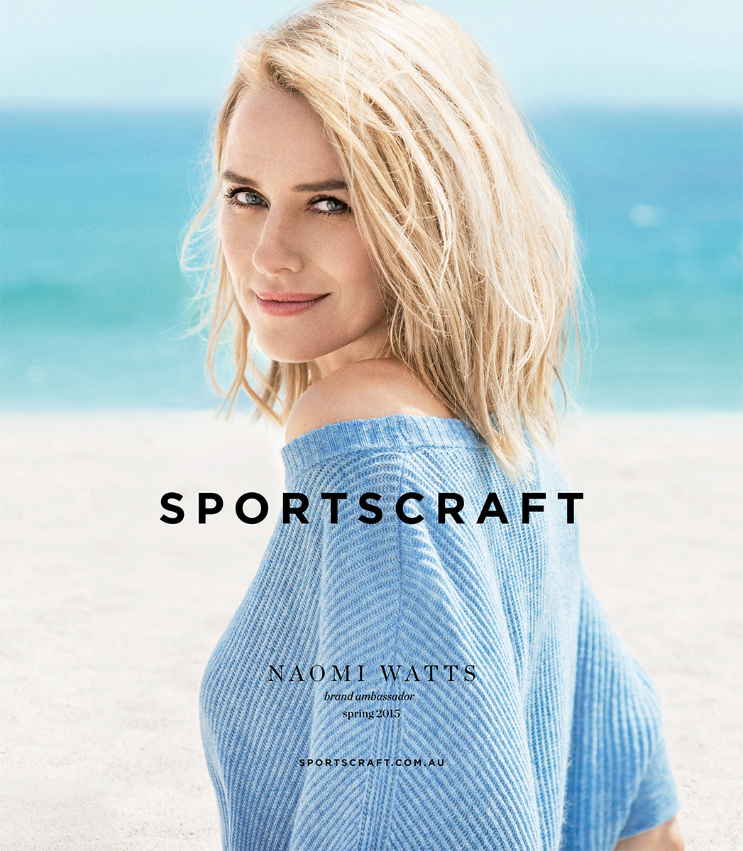 Blonde woman smiles in a light blue sweater in a fashion campaign image. Light blue ocean and sky in the background. Soft light.