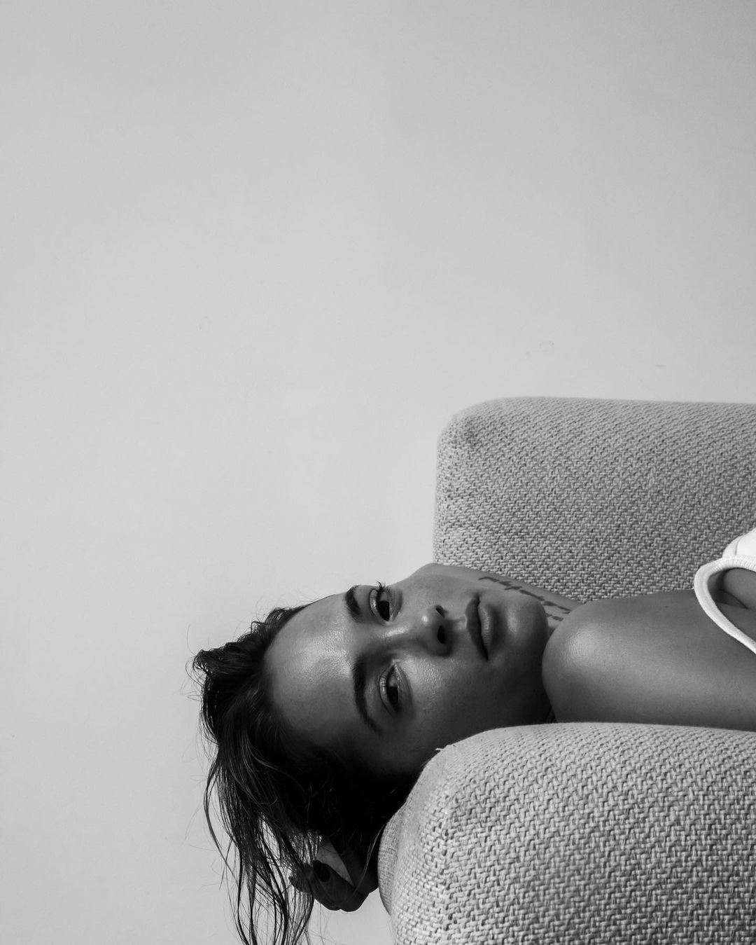 Black and white portrait of a young woman lying on a patterned couch, looking at the camera with a neutral expression.