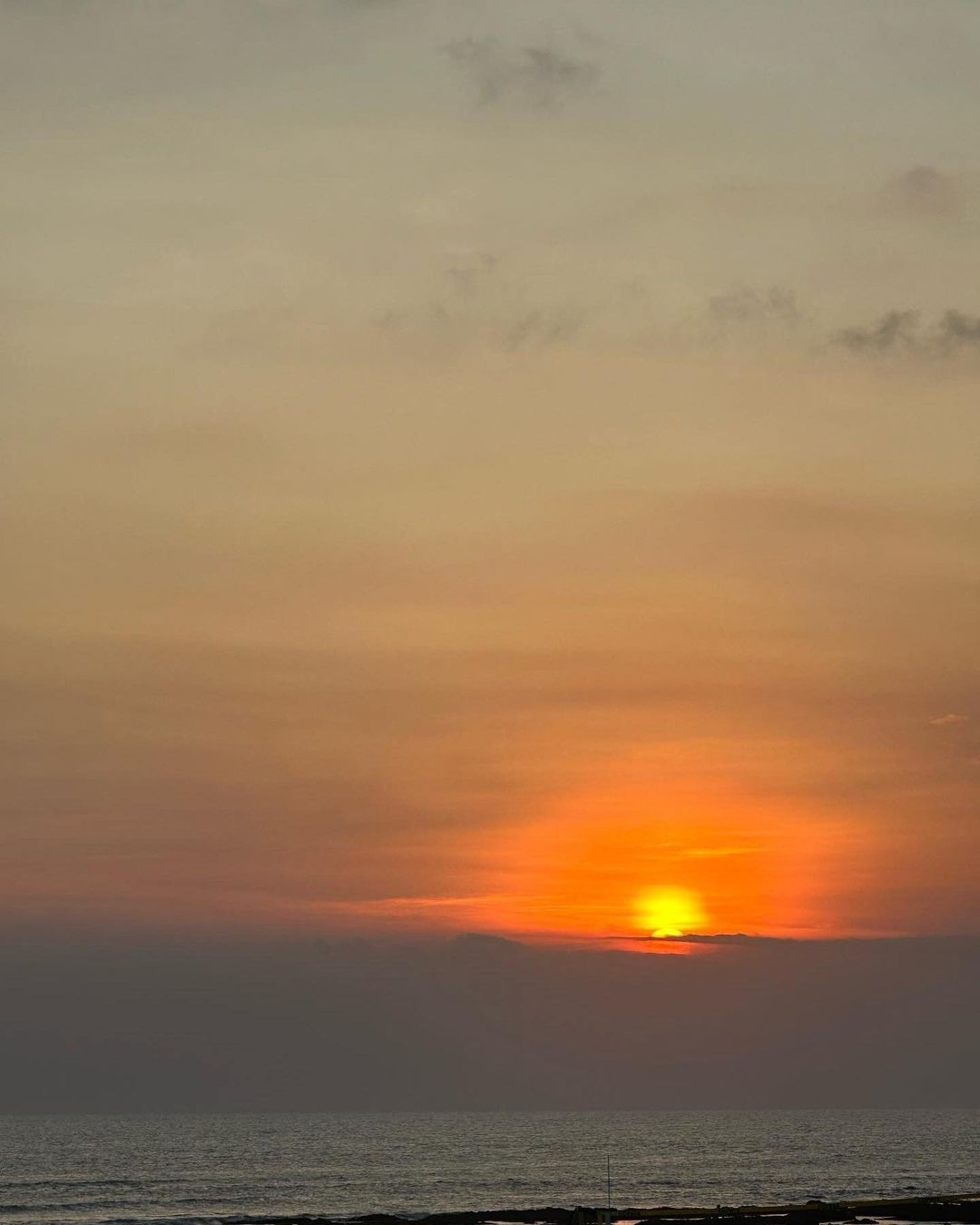 Vibrant sunset over the ocean with orange sky and clouds reflecting in the calm water. Coastal landscape at dusk.