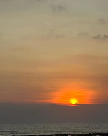 Vibrant sunset over the ocean with orange sky and clouds reflecting in the calm water. Coastal landscape at dusk.