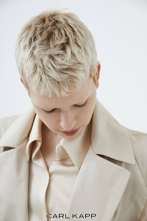 Close-up portrait of a blonde-haired model wearing a cream-colored collared shirt against a white background