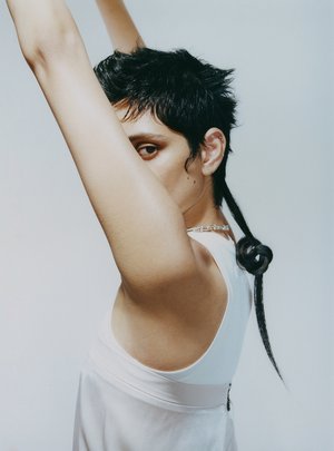 Model with dark short hair and a tied tail wearing a white sleeveless top against a seamless white studio background
