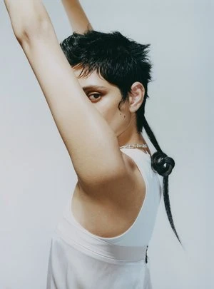 Model with dark short hair and a tied tail wearing a white sleeveless top against a seamless white studio background