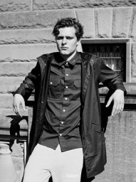 Monochrome portrait of a young man leaning against a stone wall in Sydney, styled by hair stylist Kyye.