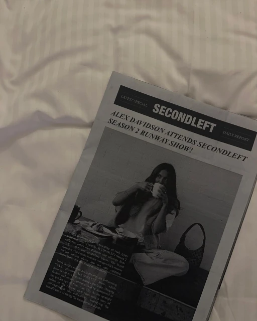 Newspaper featuring a woman drinking, lying on a white bed, conveying a relaxed morning scene with lifestyle and fashion elements.