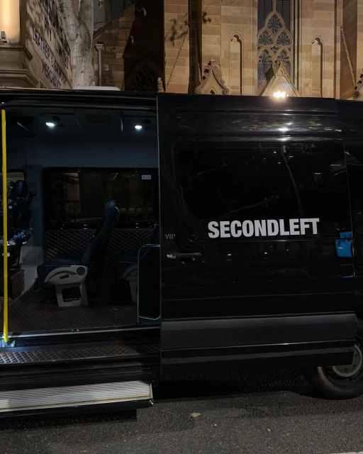 Black van with its sliding door open, revealing a glimpse of the interior, parked in an urban setting at night, illuminated by street lights.